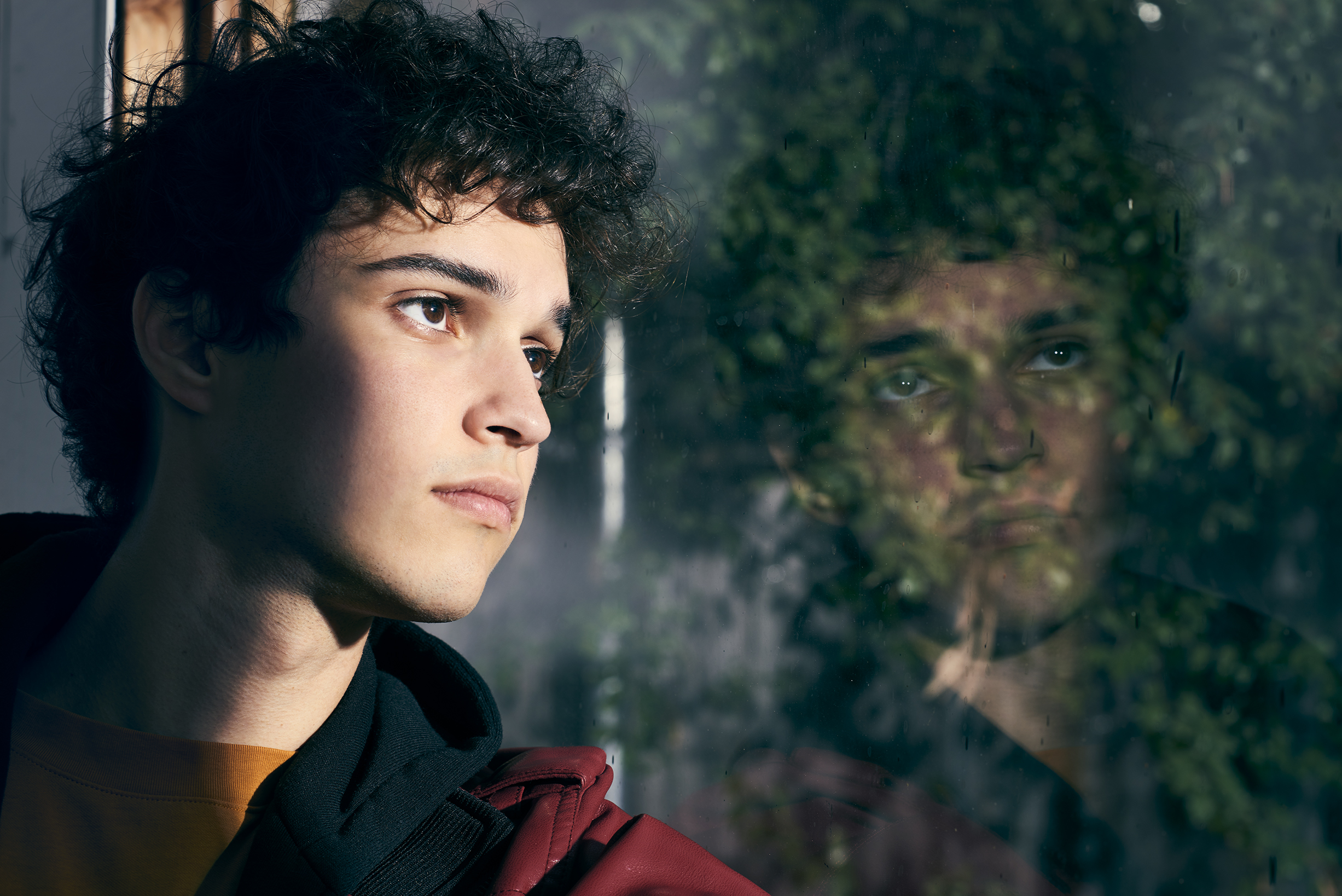 Aidan Rex Cook looking out a window with a reflected portrait in the glass